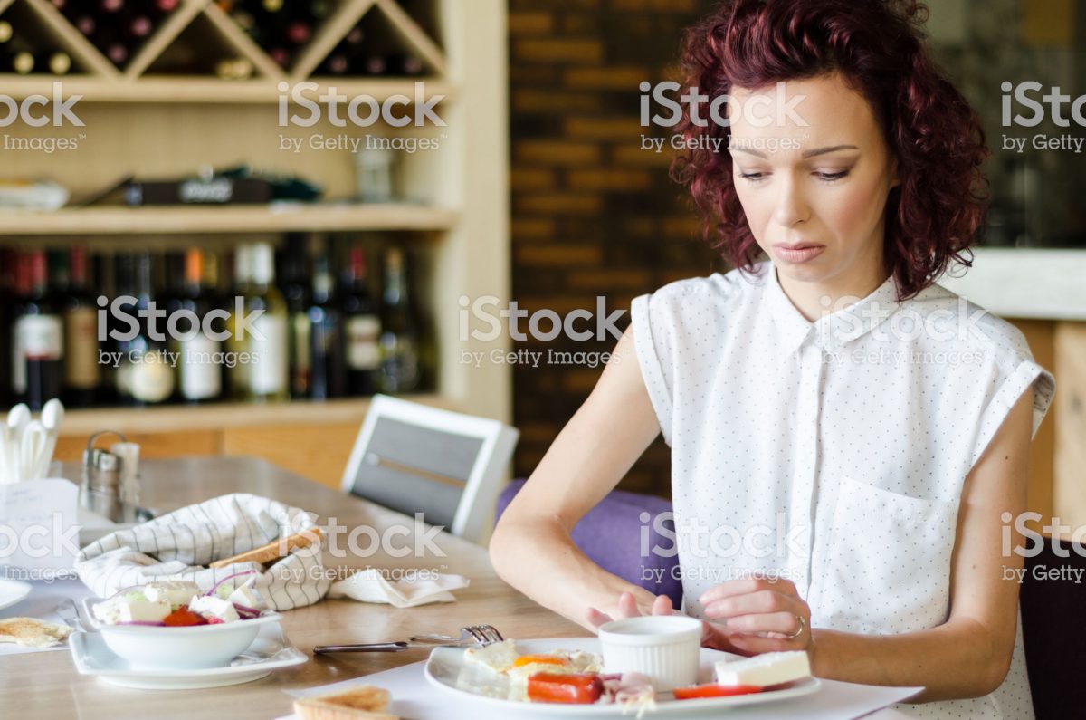 Photo of a woman looking pensively at a plate of food